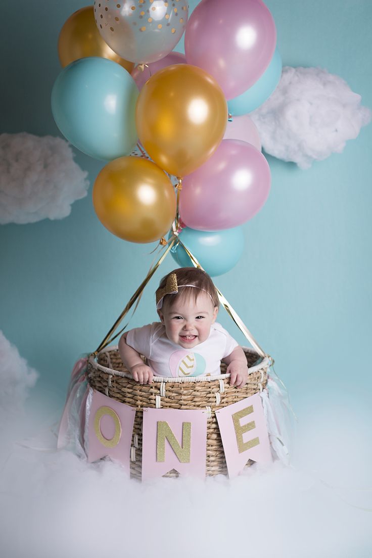 a baby is sitting in a basket with balloons on the side and one balloon above it