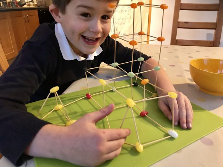 a young boy sitting at a table making a structure out of pins and plastic spoons