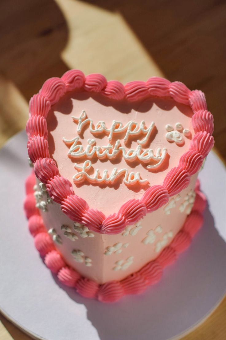 a heart shaped birthday cake sitting on top of a white plate with pink frosting