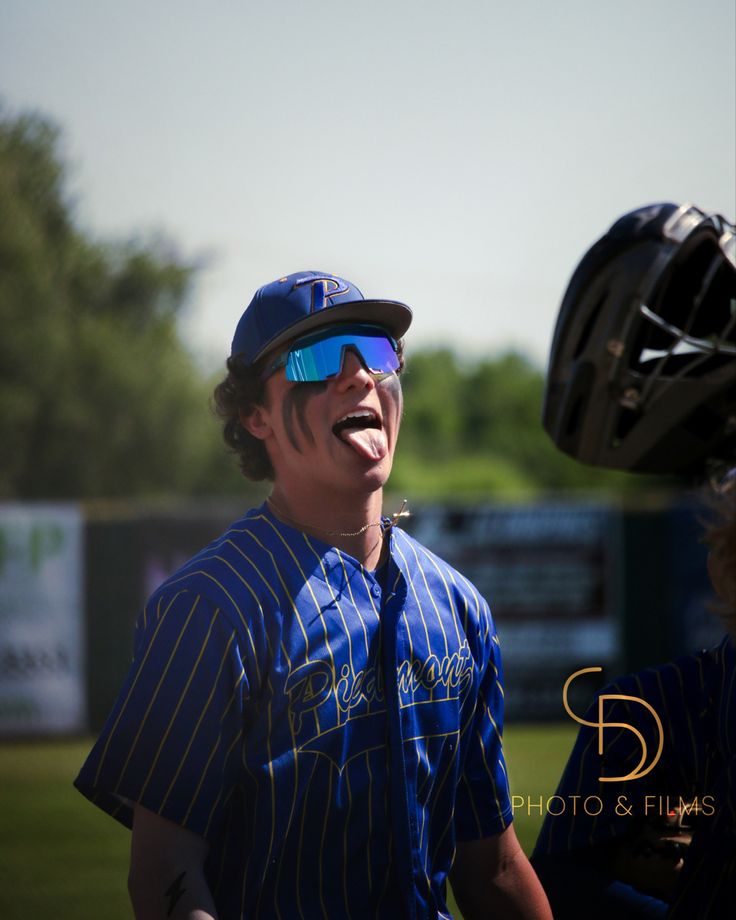 a baseball player wearing sunglasses and a blue shirt is standing in the outfield with his helmet on