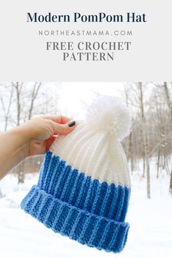 a hand holding a blue and white knitted pom - pom hat in the snow