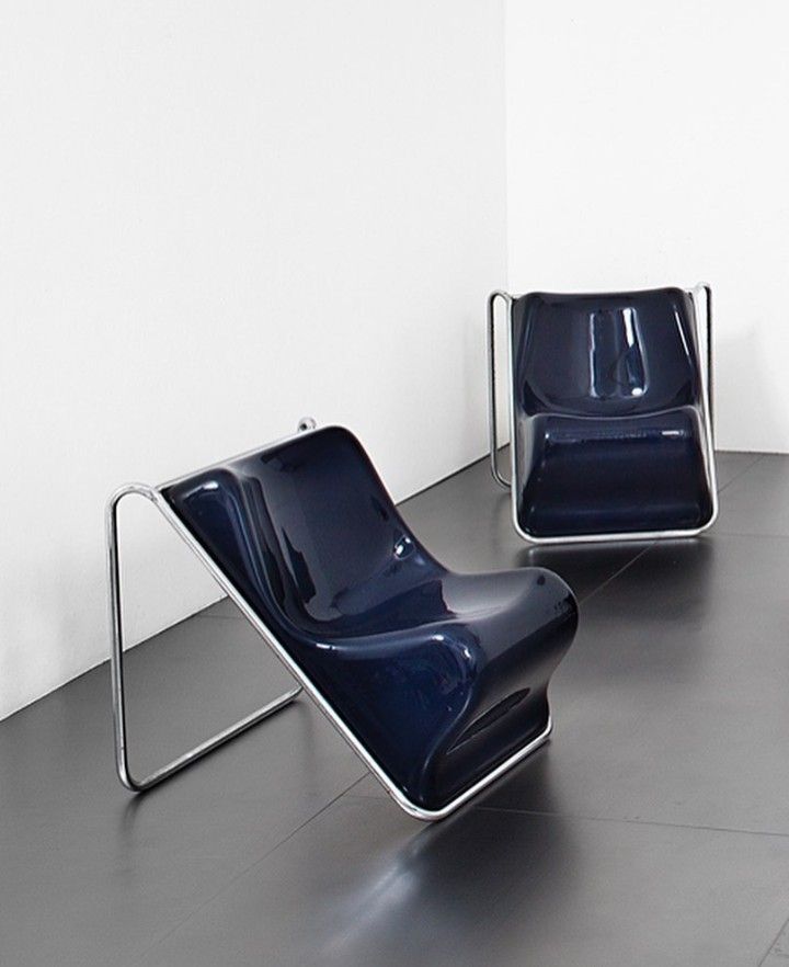 two blue chairs sitting next to each other in a white walled room with black flooring