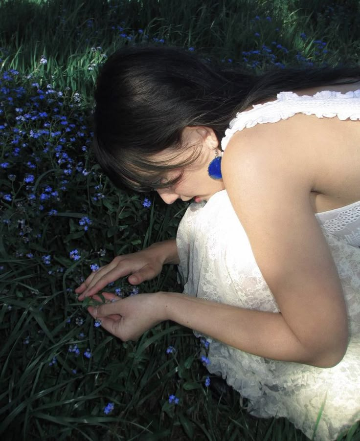 a woman kneeling down in the grass looking at something