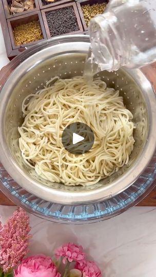 a bowl filled with noodles and water on top of a table next to pink flowers