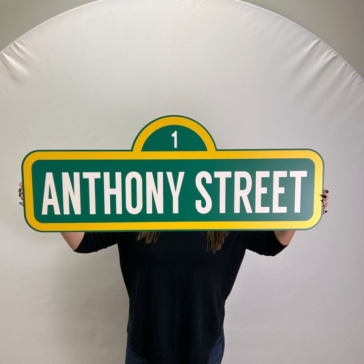 a woman holding up a sign that says anthony street in front of her face and behind her head