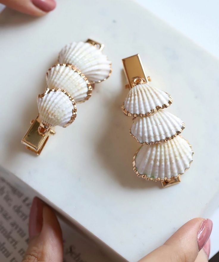 two seashells are sitting on top of a white surface and one is holding a gold - plated clip