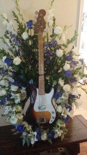 a guitar with flowers in it sitting on a table next to a vase filled with white and blue flowers