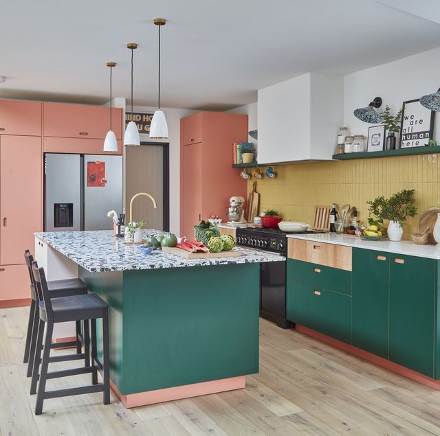 a kitchen with green and pink cabinets, an island in the middle and stools at the end