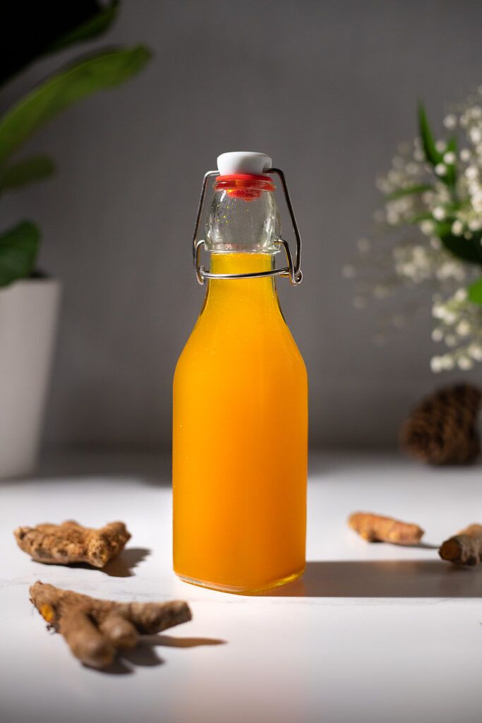 a glass bottle filled with orange juice next to some flowers