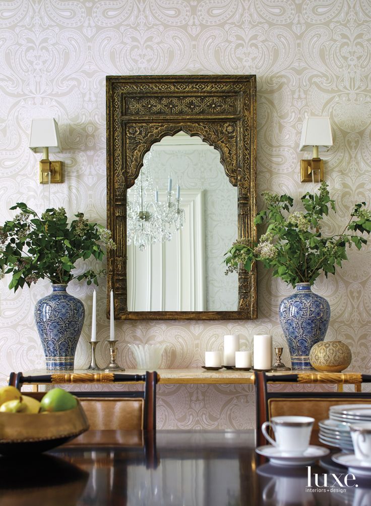 a table with two vases on it next to a mirror and some plants in front of it