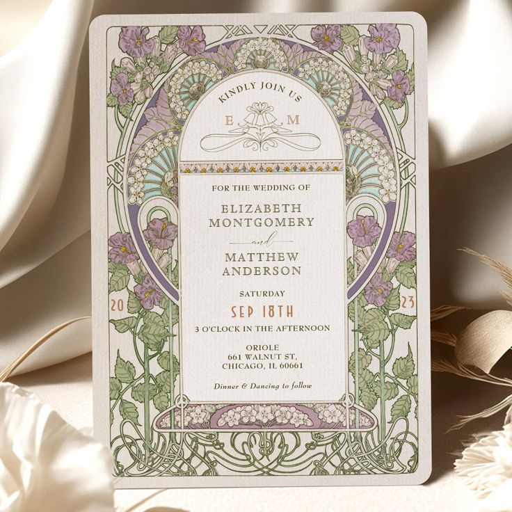 a wedding card with an ornate design on the front and back, sitting next to some flowers