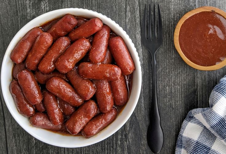 a white bowl filled with hot dogs next to a wooden spoon and fork on top of a table