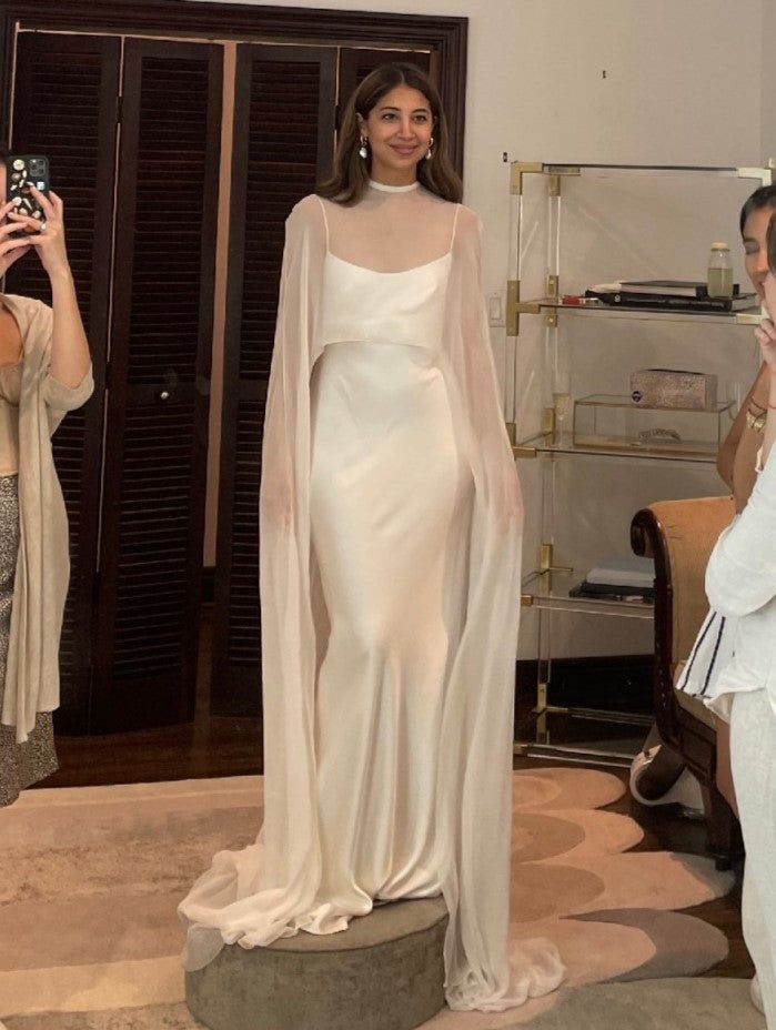 a woman taking a selfie in front of a mannequin wearing a white dress