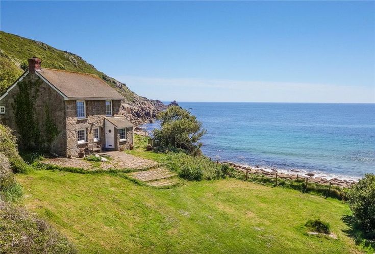 an old stone house sitting on top of a lush green hillside next to the ocean