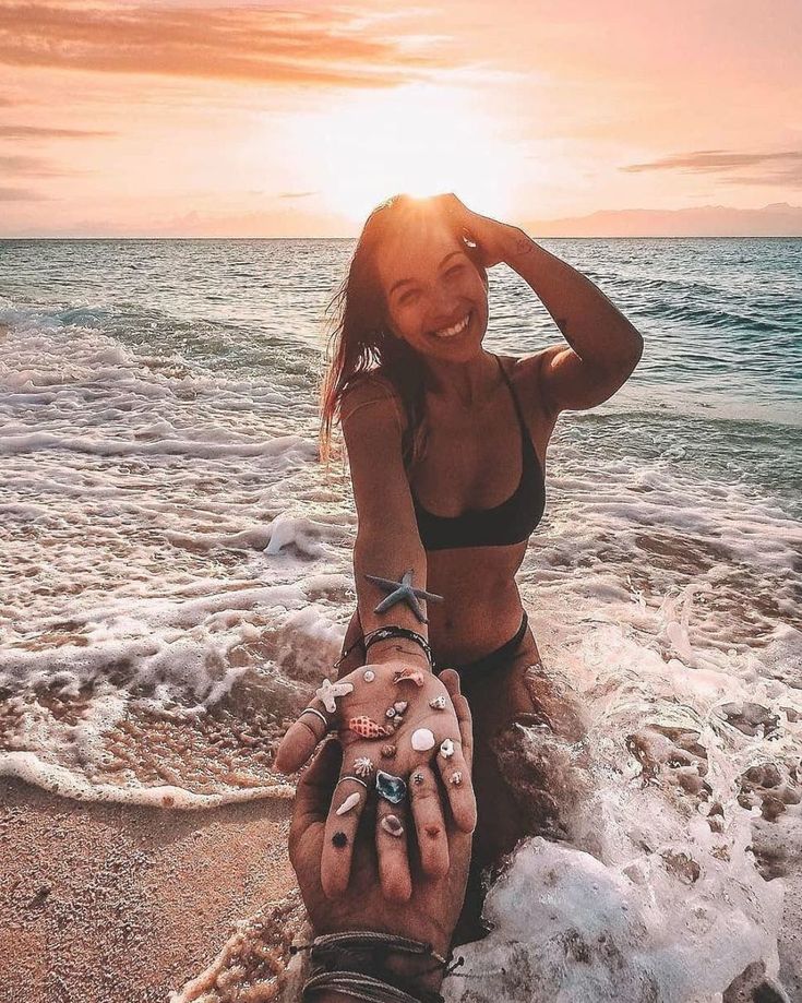 a woman sitting on the beach next to a man holding her hand with both hands