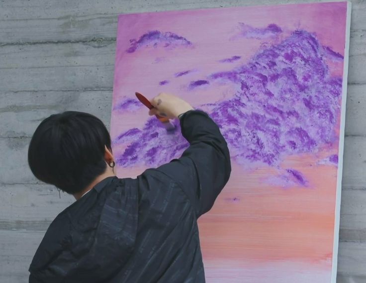 a young man is painting a mountain scene with purple and pink colors on the canvas