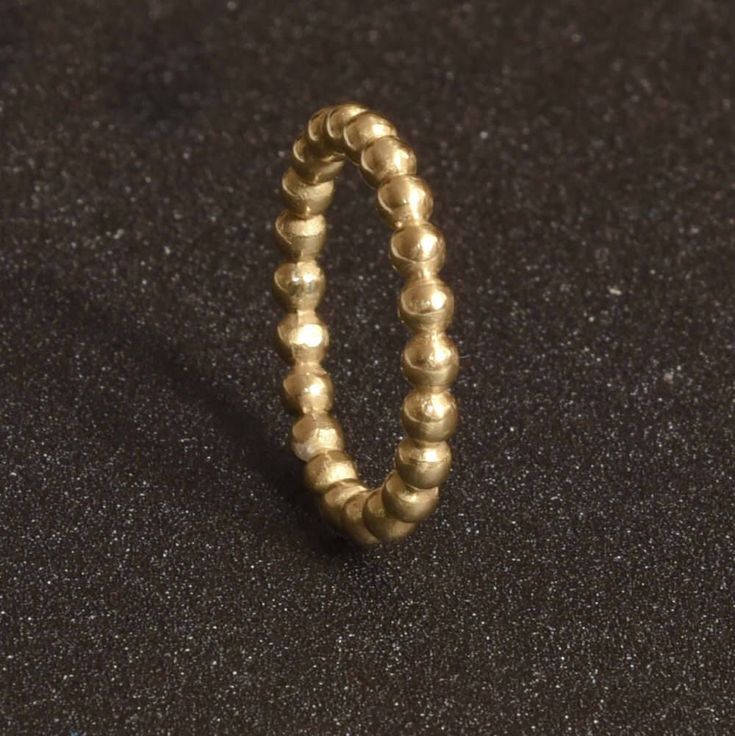 a gold beaded ring sitting on top of a black surface with a small hole in the middle