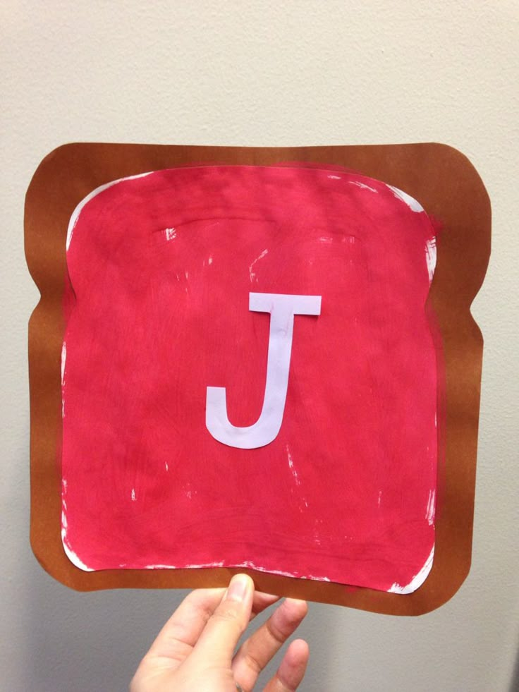 a person holding up a piece of paper with the letter j on it