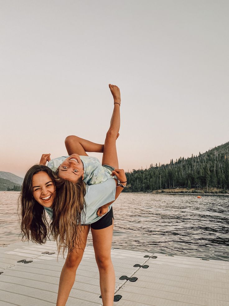 two women are posing for a photo on the dock by the water with their arms around each other