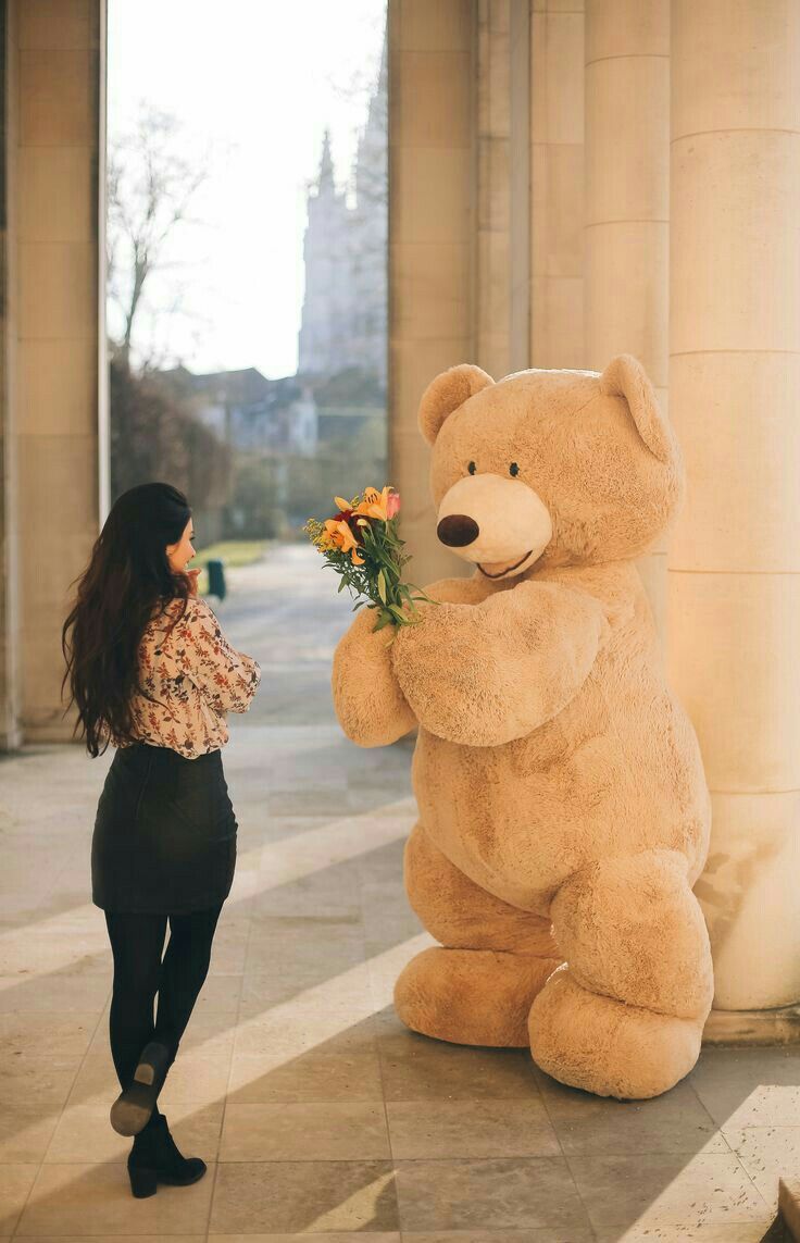 a woman standing next to a giant teddy bear with flowers in it's mouth