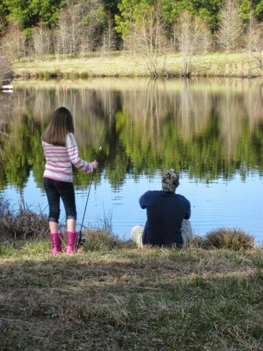 two people sitting on the bank of a lake fishing