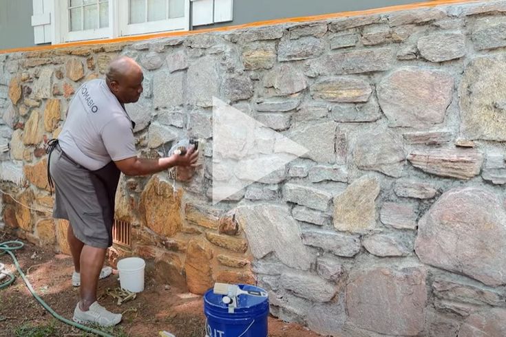 a man is painting the side of a stone wall