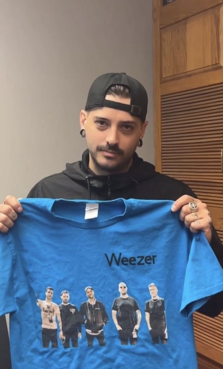 a man holding up a blue t - shirt with the words weezer on it