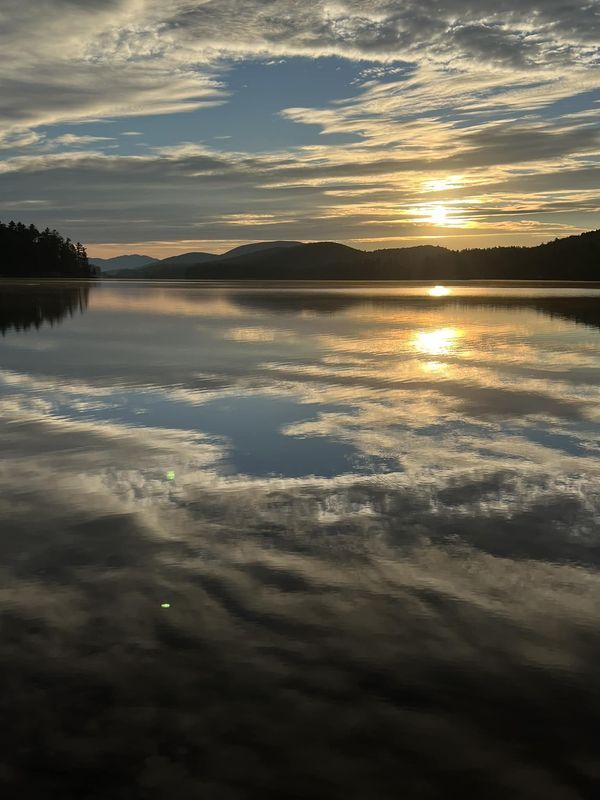 the sun is setting over a lake with mountains in the distance and clouds reflected in the water