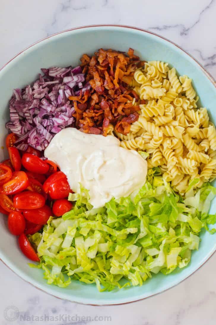 a bowl filled with pasta, lettuce, tomatoes and other ingredients on top of a marble counter