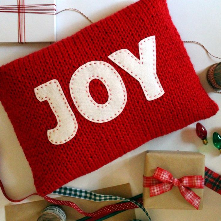 a red knitted pillow with the word joy on it next to some crafting supplies