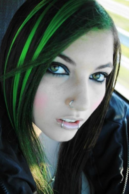 a woman with green hair and piercings on her nose is sitting in a car