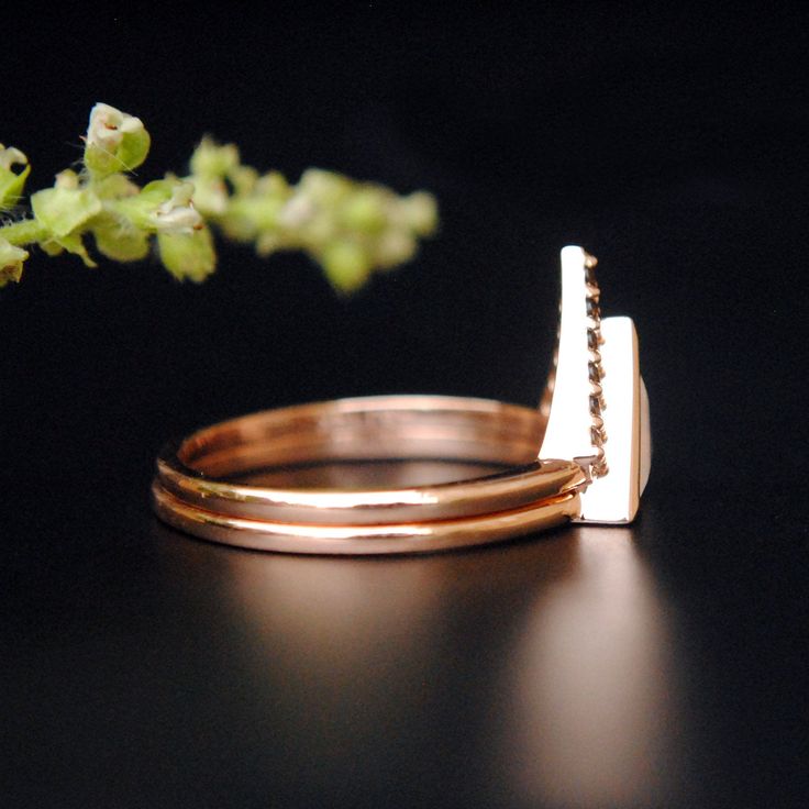 two gold wedding rings sitting on top of a table next to a branch with flowers