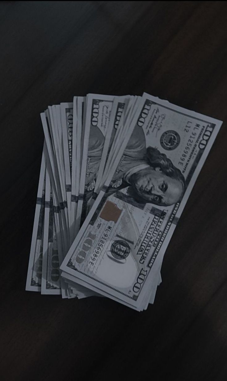 several stacks of money sitting on top of a wooden table next to a cell phone