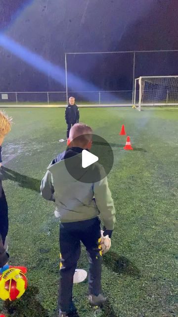 two young boys playing soccer on a field at night with lights and cones in the background