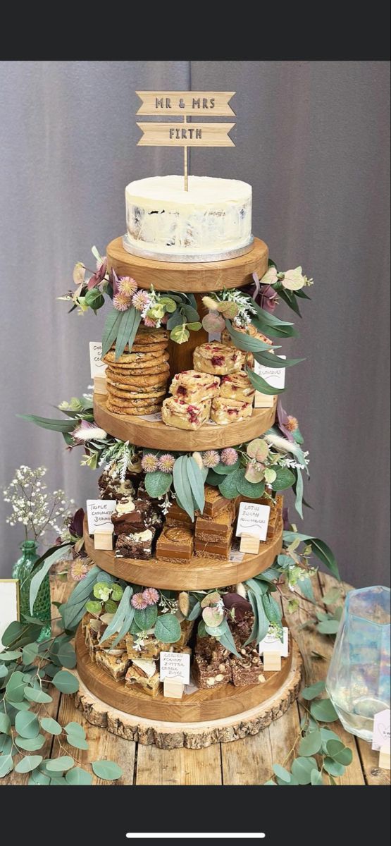 a three tiered cake with flowers and greenery on the top is surrounded by other desserts