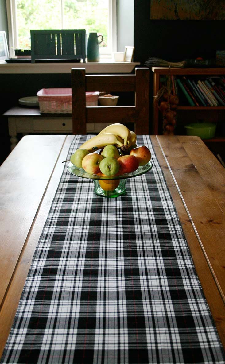 apples and pears in a glass bowl on a plaid table runner at the end of a dining room table