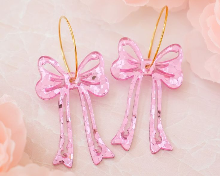 These pink sequin bow earrings are the perfect accessory to add an extra pop to your outfit! Acrylic is very lightweight so you can enjoy large, statement earrings comfortably all day. ♡ Made with pink sequin acrylic ♡ Size: Approximately 2.5 inches in length measured from earring hoop  ♡ Choice of 18k gold plated brass or stainless steel earring hoop ♡ Care Instructions: ♡ - To clean: Wipe with a microfiber cloth to remove any dust - Avoid contact with perfumes and lotions as these can react with acrylic and cause discoloration in some cases. We recommend putting on your earrings after getting ready - Although acrylic jewelry is durable, it is still a delicate material. We recommend storing them on a jewelry stand or box when not in use. - Avoid wearing or submerging in water, please don' Large Statement Earrings, Earring Hoop, Valentines Earrings, Sequin Bow, Bow Jewelry, Acrylic Jewellery, Bow Earrings, Custom Earrings, Valentines Gifts For Her