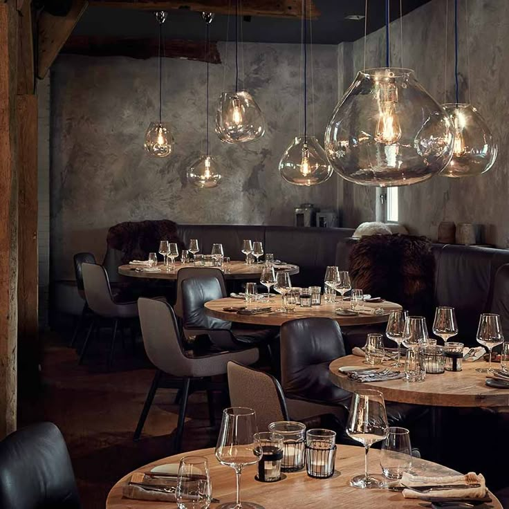 a restaurant with tables and chairs, lights hanging from the ceiling above them are empty wine glasses