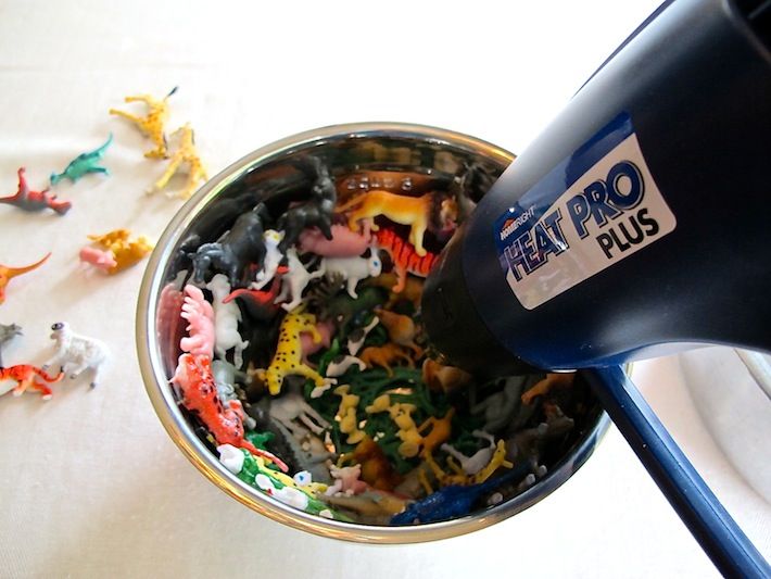 there are many toy dinosaurs in the bowl and one is pouring them into the cup