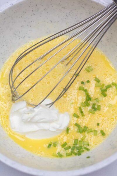 a bowl filled with eggs, sour cream and green onions next to a whisk