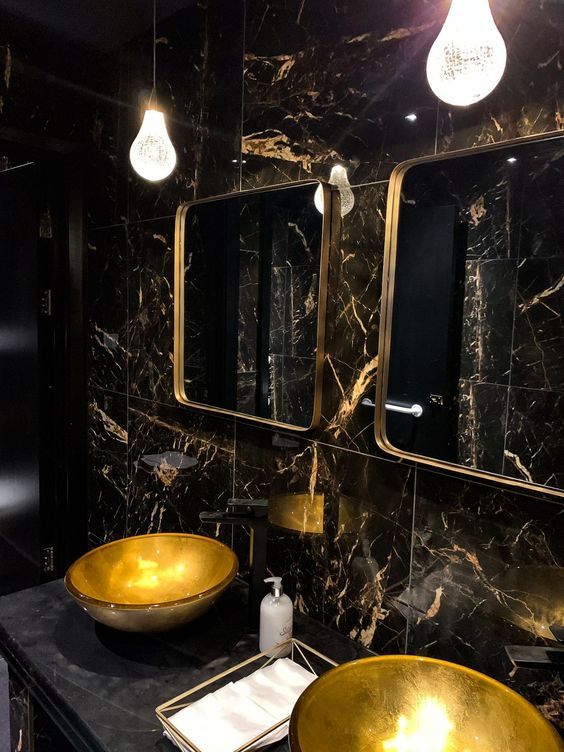 a bathroom with two gold sinks and black marble counter tops, along with three lights hanging from the ceiling