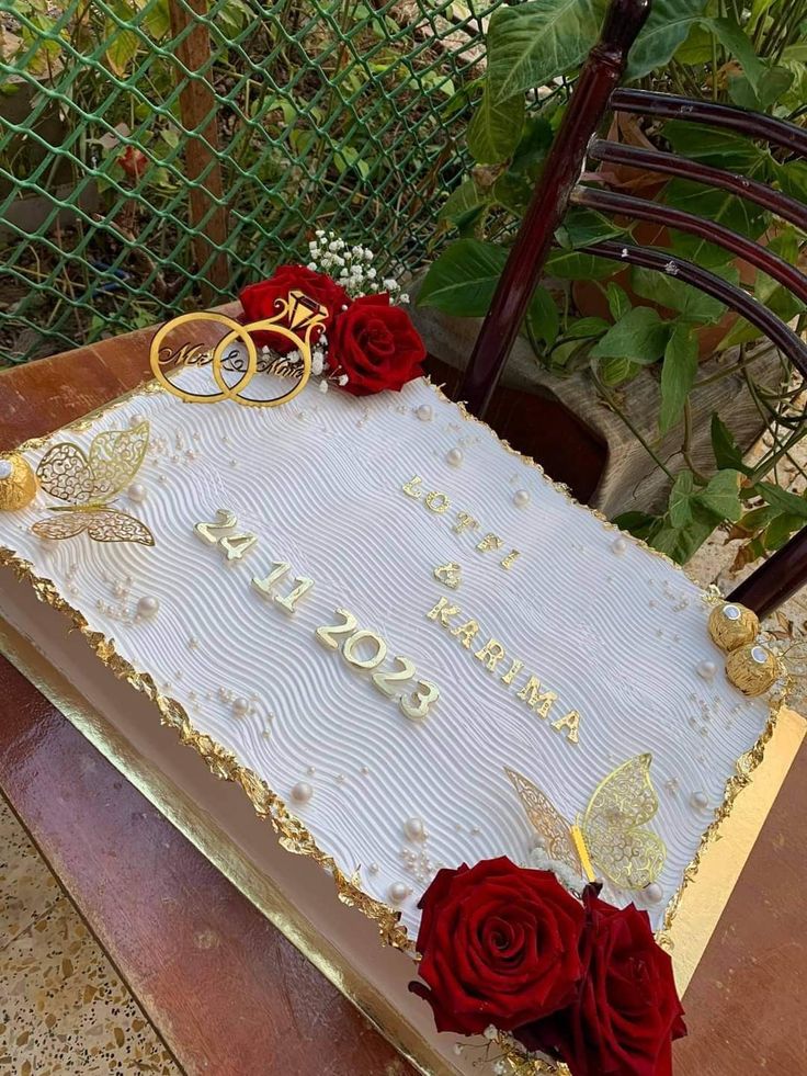 a sheet cake decorated with roses and two gold wedding rings on the top is sitting on a wooden table