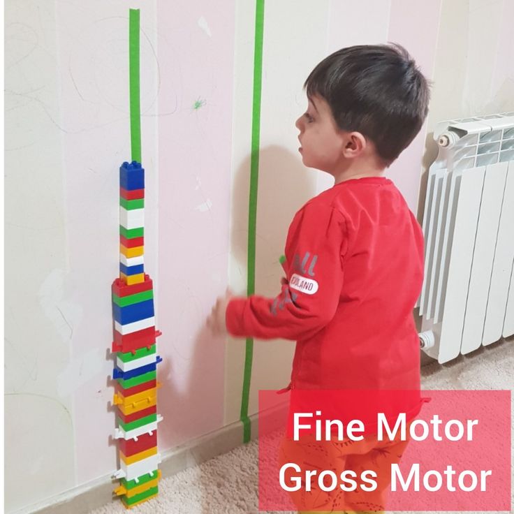 a little boy standing next to a tall stack of colored blocks with the words fine motor gross motor written on it