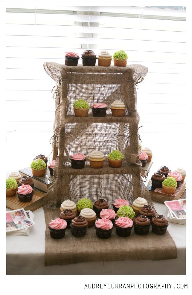 a table topped with cupcakes and cakes on top of a wooden stand next to a window