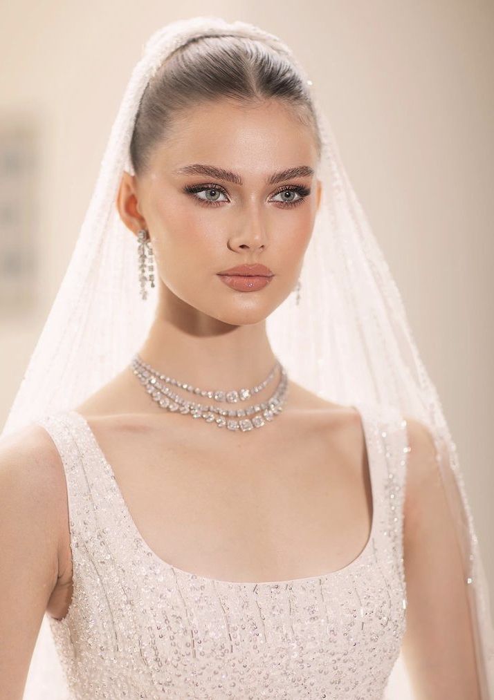 a woman in a wedding dress with a veil on her head and diamond jewelry around her neck