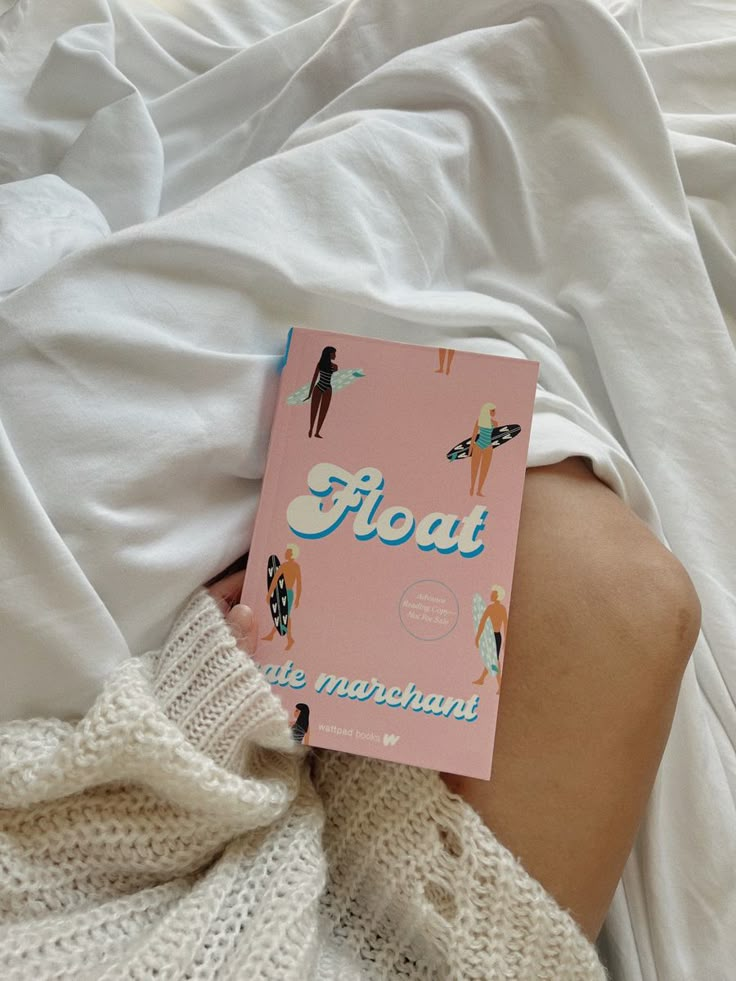 a person laying in bed with a pink book on their stomach and the cover is pulled up