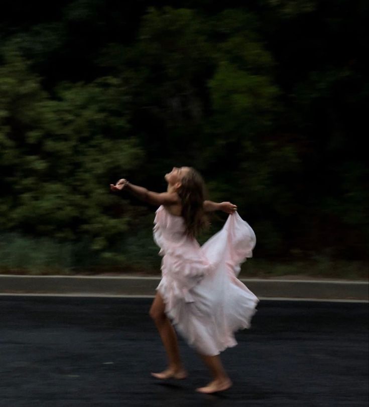 a woman in a white dress is running down the street with her arms spread out