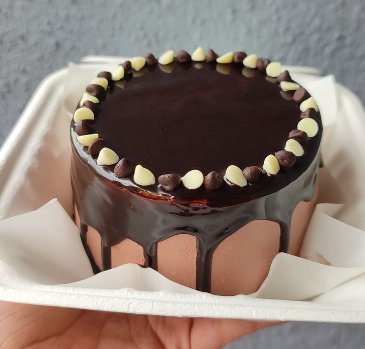 a hand holding a chocolate cake with white and brown decorations on it's top