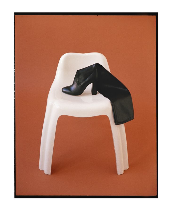 a white plastic chair with a black shoe on it's back legs, against an orange background