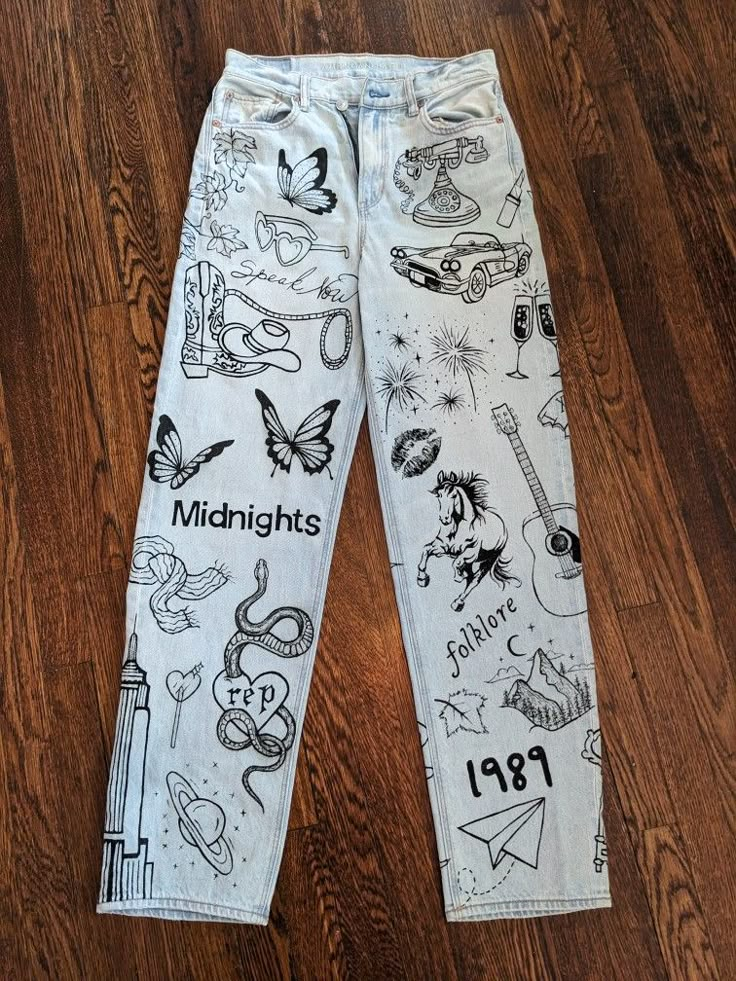 a pair of white jeans with black and white drawings on them sitting on a wooden floor